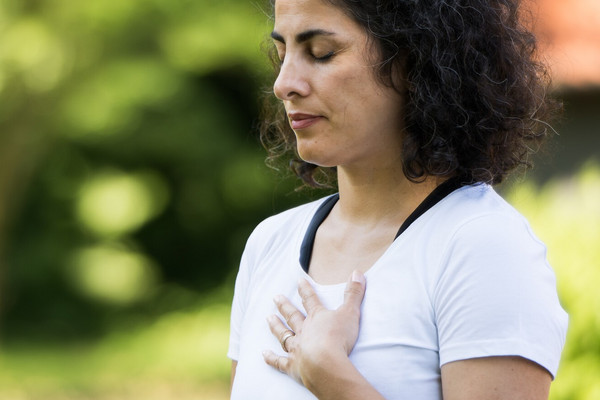 frau steht mit geschlossenen Augen und Hand auf der Brust im grünen