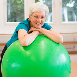 Eine ältere Dame liegt mit verschränkten Armen auf einem Gymnastikball.
